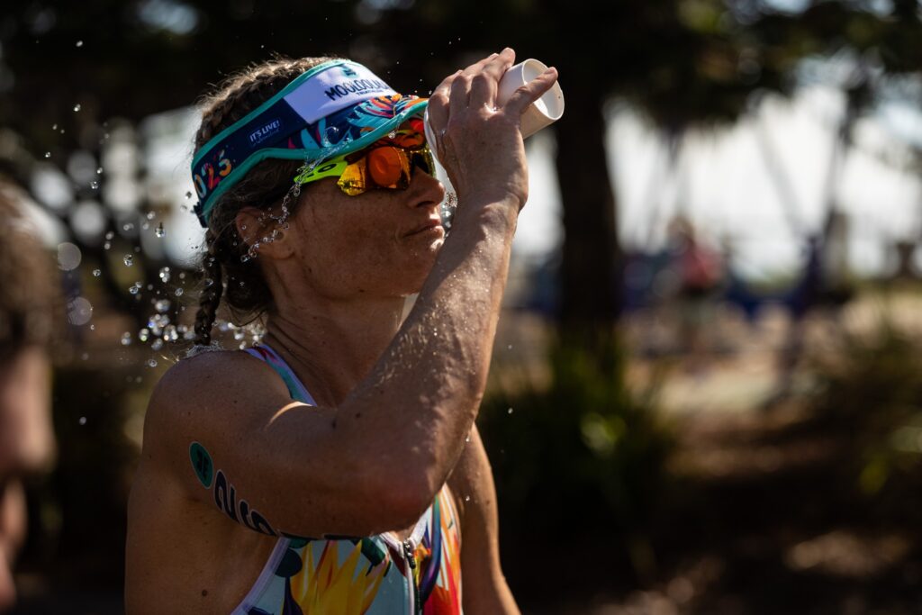 Female triathlete at the Noosa Triathlon wearing a tri suit and a custom visor pouring water on her face. 