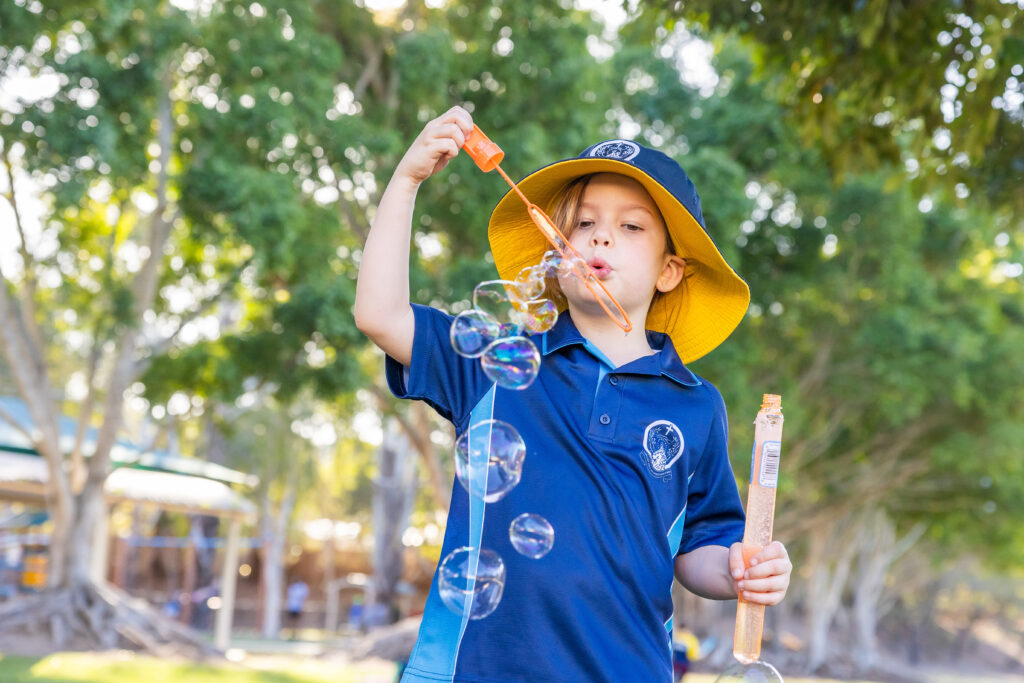 School student wearing a custom hat and school uniform whilst blowing bubbles.
